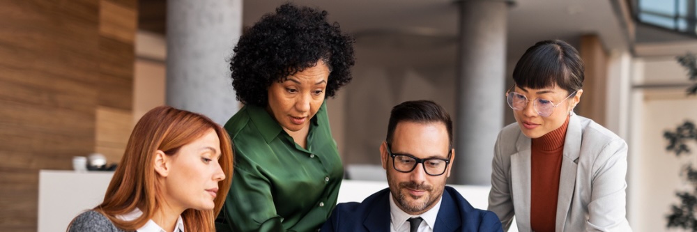 Photo of two women looking over the shoulder of a man and a computer
