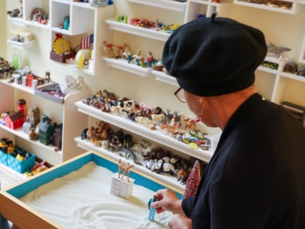 Therapist guiding sand‑tray play therapy in a room filled with miniature figurines.