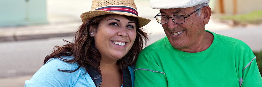 Photo of a Hispanic woman and her senior dad, smiling while traveling